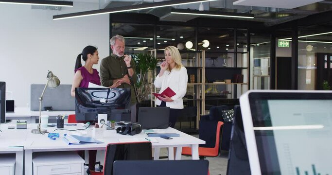 Diverse business colleagues standing using computer and discussing in office