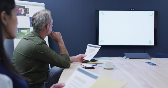 Diverse business colleagues sitting looking at screen in office meeting