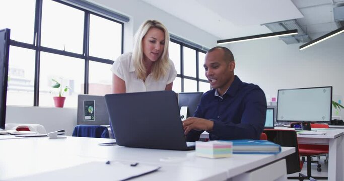 Diverse business colleagues talking at desk using laptop in office