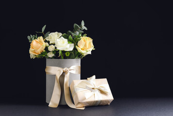 Box with beautiful flowers and gift on dark background