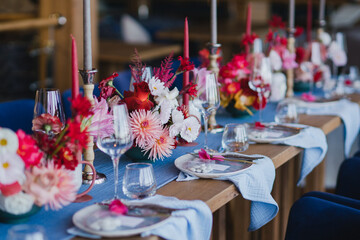 Coziness and style. Modern event design. Table setting at wedding reception. Floral compositions with beautiful flowers and greenery, candles, laying and plates on decorated table.