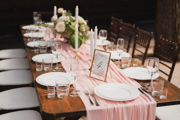 Coziness and style. Modern event design. Table setting at wedding reception. Floral compositions with beautiful flowers and greenery, candles, laying and plates on decorated table.