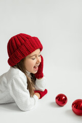 Cute little girl in a red hat with christmas decorations on a white background.  The child laughs loudly.