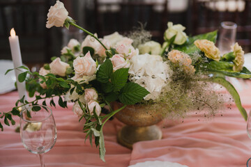 Coziness and style. Modern event design. Table setting at wedding reception. Floral compositions with beautiful flowers and greenery, candles, laying and plates on decorated table.