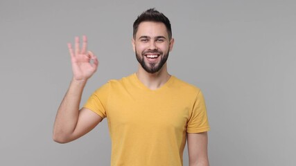 Excited cheerful amazed bearded young man 20s years old wearing yellow casual basic t-shirt isolated on grey color background studio. People lifestyle concept. Looking camera showing ok okay gesture