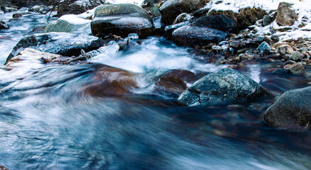 Mountain river frozen in winter with very cold blue water. The water flows down a mountain stream. Winter landscapes and background.