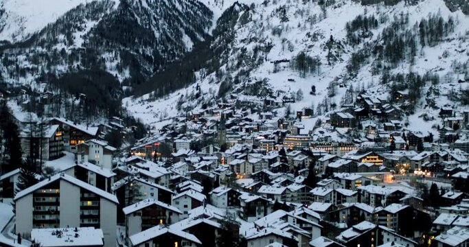 Cityscape of the Swiss village of Zermatt in Valais in winter, at dawn with snow and illuminations. The Matterhorn and the Alpine mountain range in the background.
