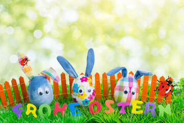 Cute 3 easter eggs as decorated easter bunnies in front of green fresh spring background in nature with colorful fence and fresh background.
