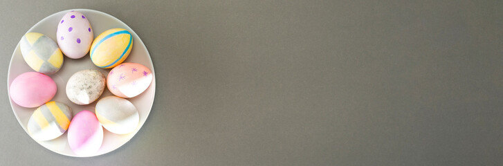 Easter eggs on a gray plate on a gray background with place for text. Top view, banner