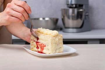 Piece of cake with vanilla and berry cream. Female hand with dessert spoon near the pie.