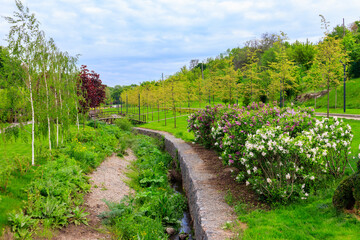 Beautiful view of the city park with arched footbridge across small river and young trees