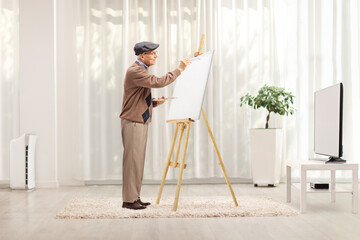 Elderly male artist painting on a canvas at home