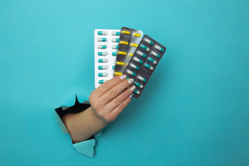 Woman hand giving a blister of pills through a hole torn in blue paper wall. Health care and...