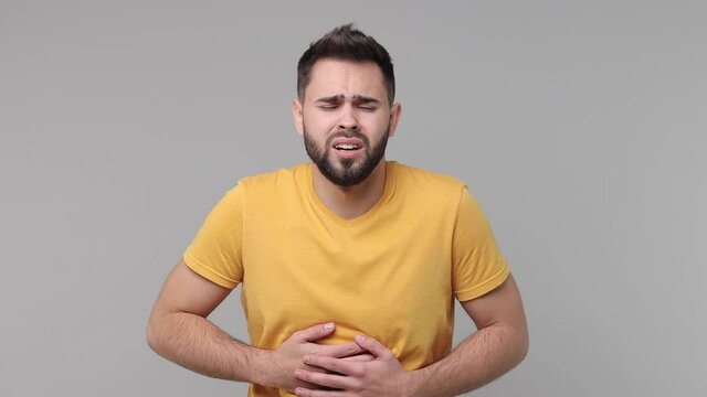 Sick ill bearded young man 20s years old in yellow casual t-shirt isolated on grey background studio. People lifestyle concept. Put hands on abdomen with stomach-ache griping bellyache feel bad seedy