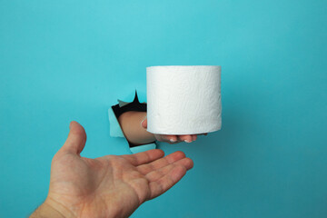 Female hand out of hole in the paperman, holding a roll of toilet paper.