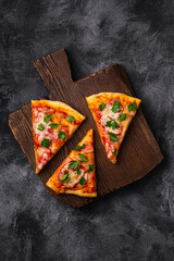 Hot pizza slices with mozzarella cheese, ham, tomato and parsley on brown wooden cutting board, stone concrete background, top view