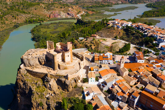 Scenic aerial view of medieval Cofrentes Castle towering over city residential buildings atop rocky cliff over Cabriel River, Valencia, Spain