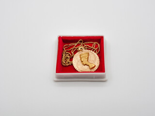 Gold jewelry, a female pendant in the form of a portrait of Cleopatra with a gold-plated chain on a red cushion in a jewelry case.