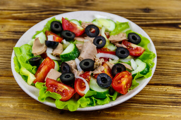 Tasty tuna salad with lettuce, black olives and fresh vegetables on wooden table