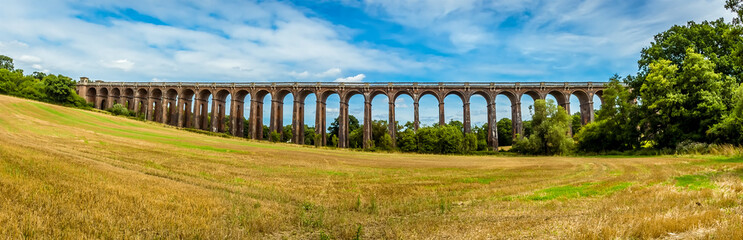 Fototapeta premium A view from the lower side of a field towards the Ouse Valley viaduct in Sussex, UK on a summers day
