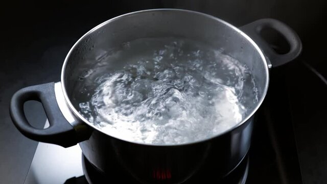 Boil water in a pot on dark background