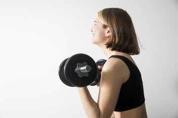 A nineteen-year-old smiling girl with a bob hairstyle and bleached strands in a gray short top holds a dumbbell
