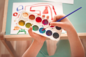 children's hands with palette of watercolors and brush, slective focus,