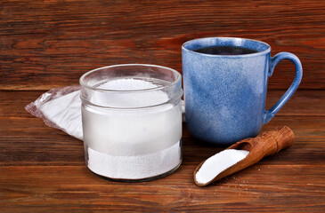 Fructose in a transparent pack with cup of tea, glass jar and scoop of sorbitol on a wooden background. Different sweeteners concept.