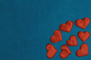 Red textile hearts in corner on blue cardboard background. Valentines Day concept, copy space, flat lay.