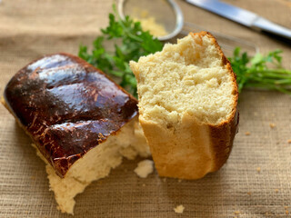 Cornbread is broken in half. A loaf of bread on burlap. Greens for dinner. Daylight from the window.