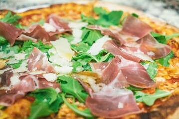Pizza from the oven. Oven-baked pizza with Italian ham and arugula close up