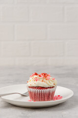 Red velvet cupcakes with cream cheese icing are decorated for Valentine's Day on a white plate on a...