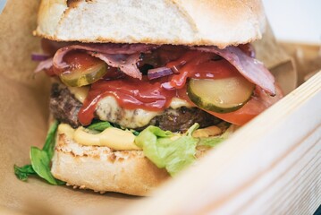Burger with fries , bacon and vegetables on a board. Dinner main dish on a wooden table
