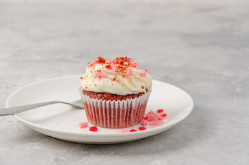 Red velvet cupcakes with cream cheese icing are decorated for Valentine's Day on a white plate on a gray background. Copy space.