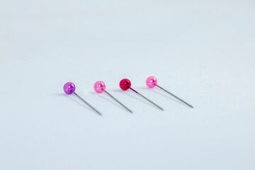 Vier Stecknadeln in den Farben lila, pink und rot liegen nebeneinander.