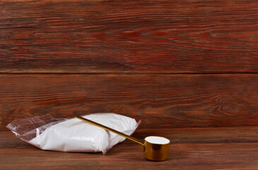 Fructose in a transparent pack with golden spoon of sorbitol on a wooden background. Different sweeteners concept.