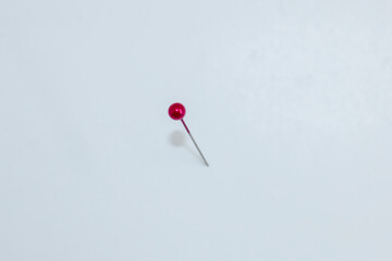 Rote Stecknadel steckt im Untergrund und wirft einen Schatten.