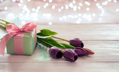A gift and a bouquet of tulips on the background of a burning garland. Side view with copy space. The concept of holiday backgrounds.