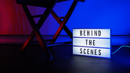 Behind the scenes letterboard text on Lightbox or Cinema Light box. Movie clapperboard megaphone and director chair beside. Background LED color change loop. static camera in video production studio.