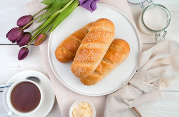 Bread on a flat plate, tulips and tea on a light wooden background. The view from the top. The concept of festive culinary backgrounds.