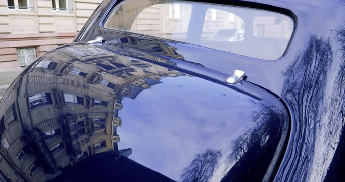 Rear view of an retro old vintage car with typical Haussmannian building reflected in the shiny paint of the car