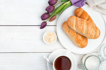 Fresh loaf, butter, a bouquet of tulips and tea on a light wooden background. Side view with copy space. The concept of festive culinary backgrounds.