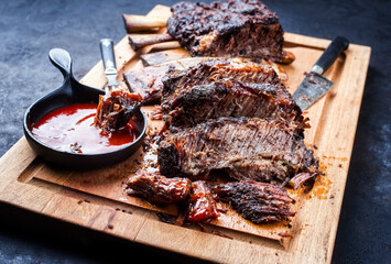Traditional barbecue burnt chuck beef ribs marinated with spicy rub and served with a hot chili sauce as closeup on a rustic wooden cutting board