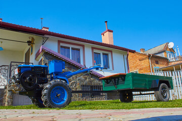 Obraz premium new tractor with trailer,on the background of the house bought a new two-wheeled tractor for agriculture