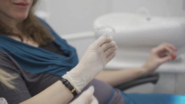 Orthodontist holding invisible retainer for teeth alignment. In clinic shows patient modern dental technology - removable transparent plastic aligners or invisalign use and benefit. Close up on hand