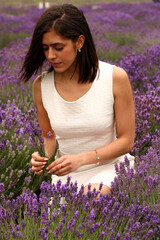 Hispanic girl of short brown hair in white dress picking up lavender flowers in a field during spring