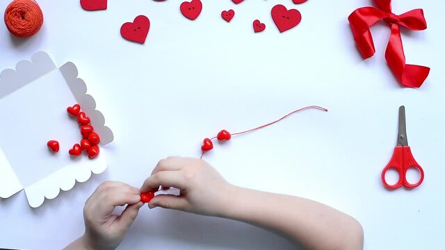 DIY baby pens string red beads hearts on strings for valentine's day bracelet. handmade baby decoration. handicraft concept. step 3.Layout, top view.