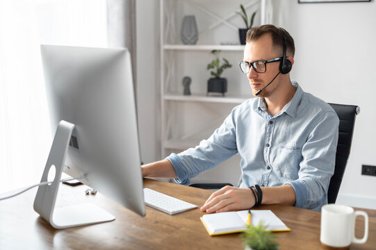 A Confident Businessman, Office Employee, Call Center Worker Is Using Hands Free Headset For Talking Online, Video Communication. A Pleasant Guy Looks At Webcam And Speaking