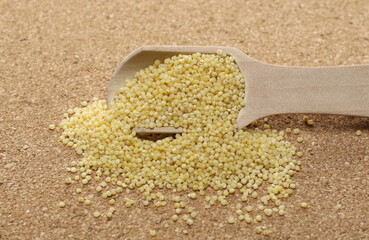 Peeled yellow millet seeds with wooden spoon, organic food product on cork background, macro
