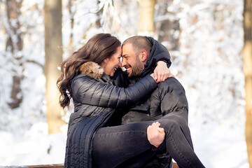 Man and woman in love hugging and kissing on a bridge. Snowy winter background.